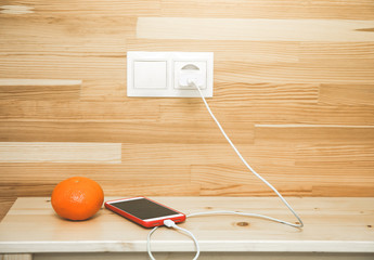 Smartphone and orange are lying on the bedside table. Stylish minimalist photo. Mobile is charging.