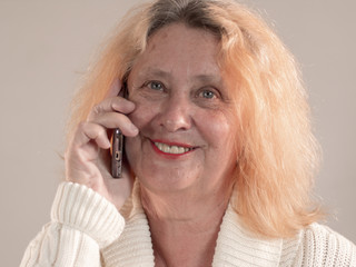 Cheerful elderly woman with red hair and wrinkled face is talking on phone and sends message. pensioner monitors screen of smartphone