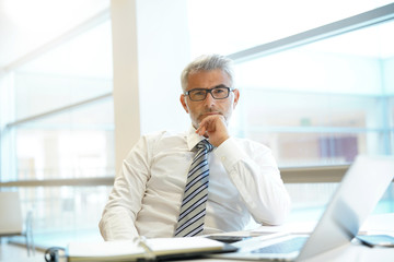 Portrait of mature businessman sitting at desk looking into camera