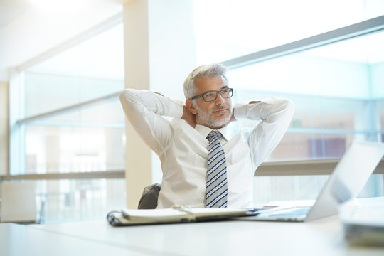 Relaxed businessman sitting at desk with arms behind head