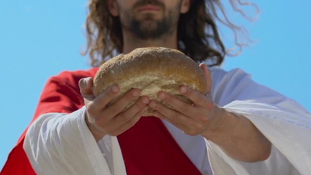 Saint Jesus in robe stretching bread into camera, gifts for poor people, charity