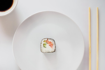 One Sushi Roll on white plate with chopsticks. Roll made of Fresh Raw Salmon, Cream Cheese and cucumber. Isolated on white background. Japanese seafood sushi roll on a white background.