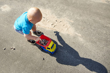 Little boy collects stones in a toy car on the pavement on a summer day