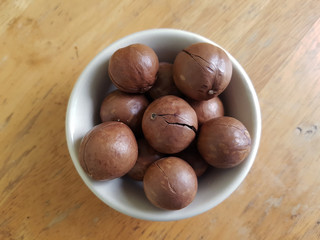 Unpeeled macadamia nuts in a white ceramic bowl on a wooden table 
