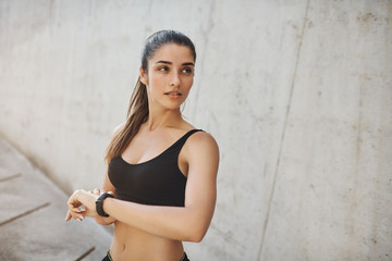 Checking vitals before running marathon. Motivated good-looking sporty woman in sports bra use fitness tracker to measure heart rate, look aside how many laps left during morning jogging session