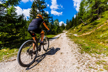 Naklejka premium Tourist cycling in Cortina d'Ampezzo, stunning rocky mountains on the background. Woman riding MTB enduro flow trail. South Tyrol province of Italy, Dolomites.