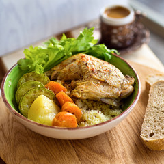 Boiled chicken leg and potatoes with zucchini, carrots and herbs served with bread and coffee on a wooden background