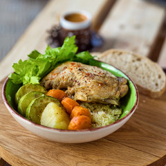 Boiled chicken leg and potatoes with zucchini, carrots and herbs served with bread and coffee on a wooden background