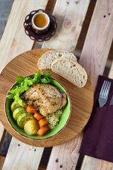 Boiled chicken leg and potatoes with zucchini, carrots and herbs served with bread and coffee on a wooden background