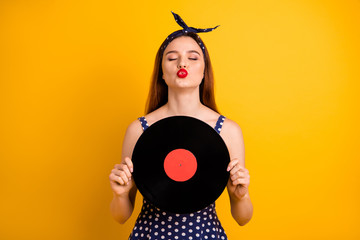 Portrait of her she nice-looking attractive lovely winsome cheerful cheery dreamy straight-haired lady holding in hands round disc sending you kiss isolated on bright vivid shine yellow background