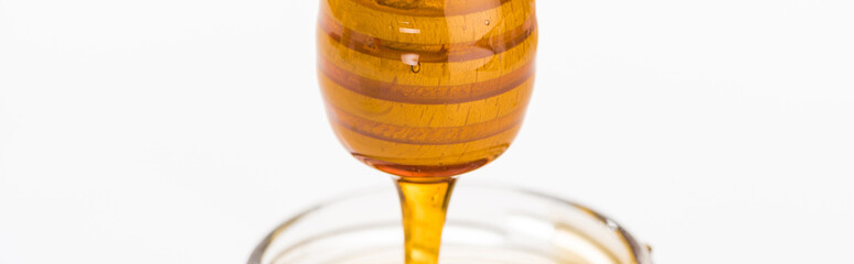 panoramic shot of wooden honey dipper with dripping honey isolated on white