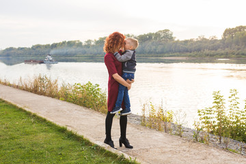 Motherhood and children concept - young mother with son in her arms near the river