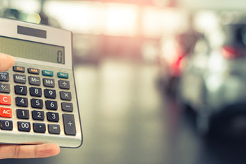 Asian man holding calculator for business finance on car showroom blurred bokeh background.for automotive automobile or transportation transport