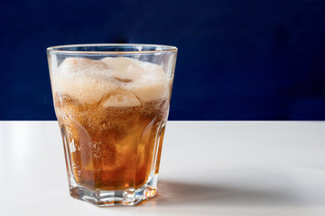 A glass of cola with ice on a white table close-up. Cold refreshing drink.