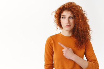 Hesitant worried cute modest redhead curly-haired female, looking pointing left dissatisfied and...