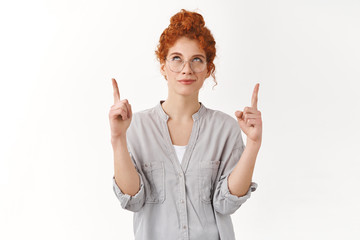 Curious cunning young redhead woman wear glasses, blouse, looking and pointing up interested, smirk...