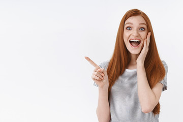 Cheerful charismatic impressed redhead young girl open mouth smiling astonished pointing upper left corner reacting awesome cool news, standing white background thrilled, fan finally come concert