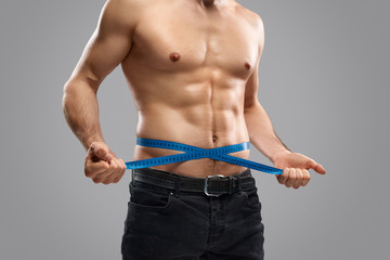 Crop slim guy measuring waistline