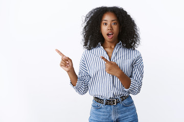 Amazed questioned african american girl seeing incredible perfomance open mouth speechless impressed asking question pointing upper left corner sideways indicating index fingers, make order fastfood