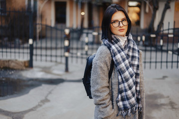 Fototapeta premium Attractive young girl wearing glasses in a coat walking on a sunny day