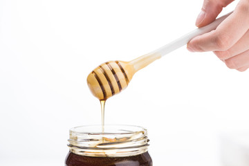 partial view of man holding honey dipper with dripping honey in jar isolated on white