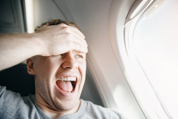 Passenger man in plane clutches his head, afraid of heights and flight. Scream and cry expression