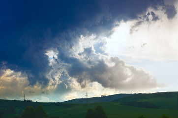Dramatic Summer Thunderstorm Clouds Over Green Hills, Trees, Power Lines on Sunset.