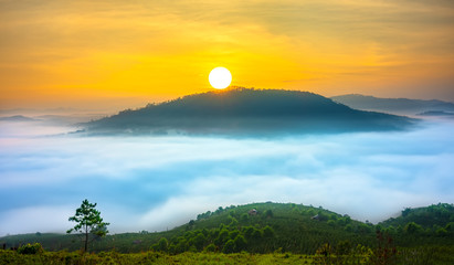Dawn on a mountain plateau Da Lat, Vietnam beneath mist covered valleys and the sun rising over sky filled yellow color. 