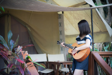 happy young cute female Asian woman Japanese girl women hipster play guitar at tent camping campfire  party at beautiful blue sky scenery river lake waterfall green forest Kanchanaburi, Thailand