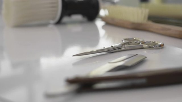 Professional tools for haircut in barbershop. Hairdressing scissors and barber accessories in hair salon. Barber picks up scissors in close-up.