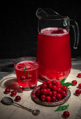 Cherry juice in a glass. Garnished with cherries. Dark wooden background. Next to a glass is a metal plate with cherry berries. In the background is a decanter with cherry juice.