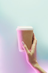Cardboard cup of coffee to go on blue and pink neon background