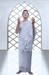 Asian Muslim man in ihram clothes standing and praying while raised arms