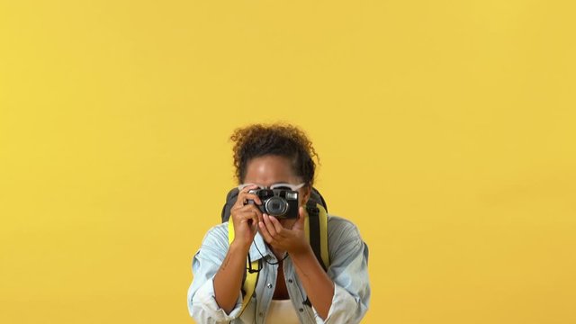 Surprised african american young woman tourist backpacker taking photos on camera against yellow backdrop