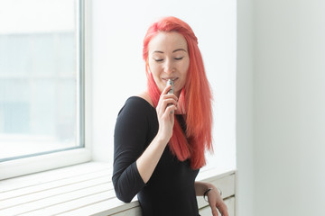 Vape, addiction and people concept - woman with red hair is smoking vape