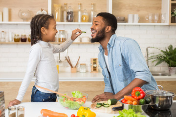 Afro girl is feeding her dad while cooking in kitchen