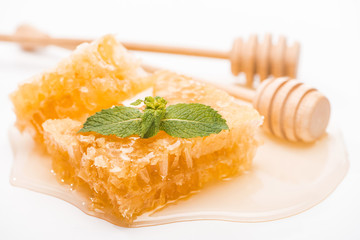 honeycomb with mint and honey near wooden honey dippers isolated on white