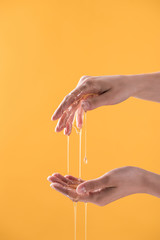 cropped view of woman showing hands in dripping honey isolated on orange
