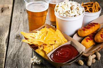 Selection of stadium game foods - nachos, pop corn, pretzels, corn dogs, rustic wood background