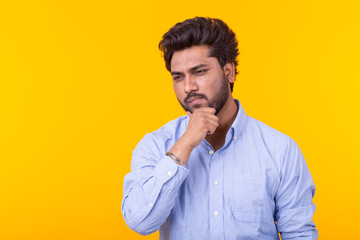 Apathetic cute young indian man is posing on a yellow background with copy space and thinking about something. Concept of unfulfilled dreams.