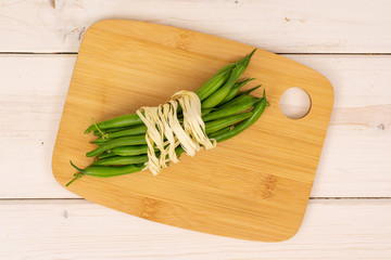 Lot of whole fresh green bean with natural bast on bamboo cutting board flatlay on white wood