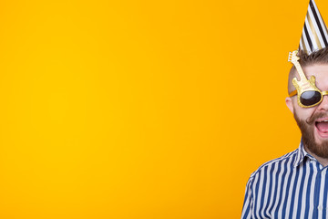 Crazy young positive hipster guy with a beard laughs happily on a yellow background with copy space. The concept of holidays and sales