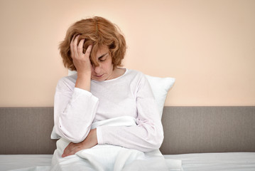 Exhausted and tired mature woman with severe headache sitting in bed and holding her head