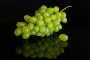Lot of whole fresh green grape one is aside isolated on black glass