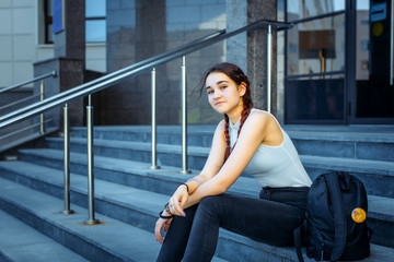 Young beautiful student sitting on the steps near the College with a backpack at recess.