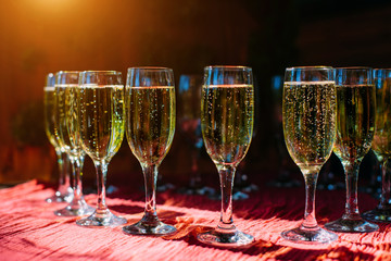 A row of glasses filled with cold champagne lined up, ready to be served. Glasses with Martini on the table - party background. Welcome drink on the wedding ceremony.