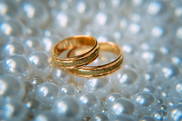 Two beautiful gold wedding rings lie among the white pearls, selective focus, close-up. Wedding concept.