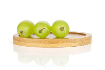 Group of three whole fresh green grape in row on round bamboo coaster isolated on white background