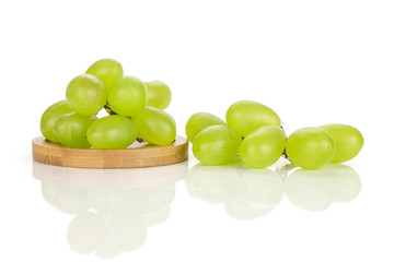 Lot of whole fresh green grape small bunch is aside on round bamboo coaster isolated on white background