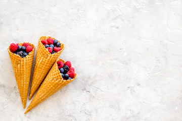 Fresh berries in waffle cones on light stone background top view mock up